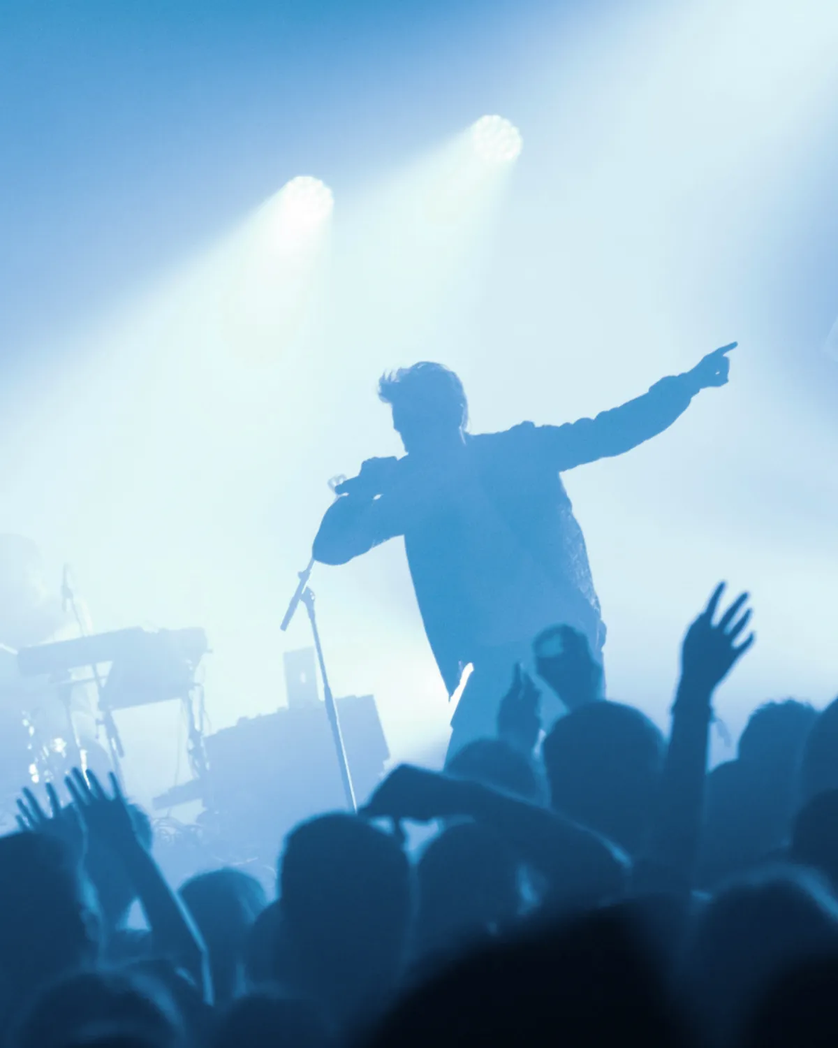 Singer silhouetted on stage under blue spotlights with crowd cheering