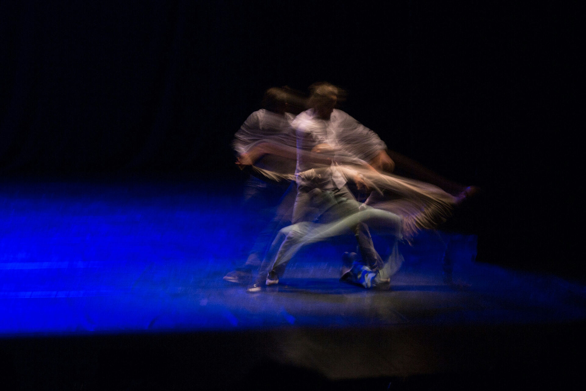 Motion-blurred dancers performing under blue stage light